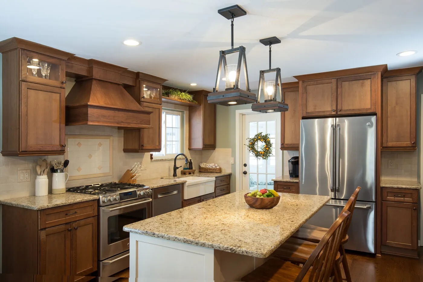 Kitchen in warm stained cabinets with a wood range hood, glass-front uppers and a painted island